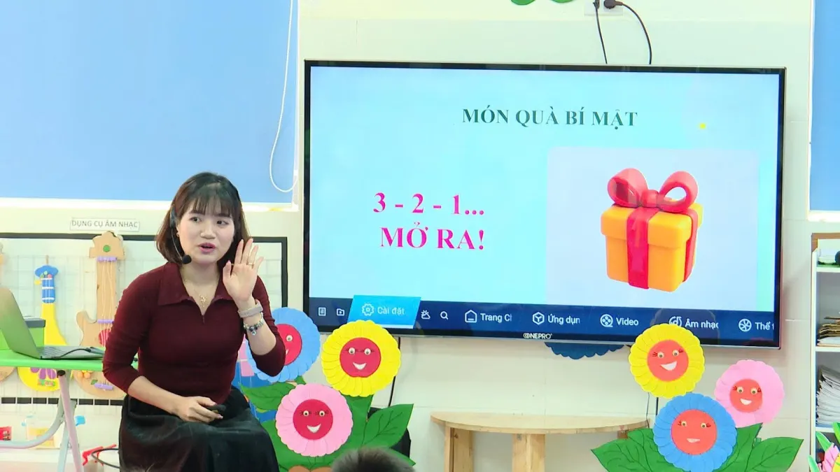 Cô Thuý Liễu đeo micro, dạy trẻ mầm non với trò chơi Món quà bí mật trên màn hình